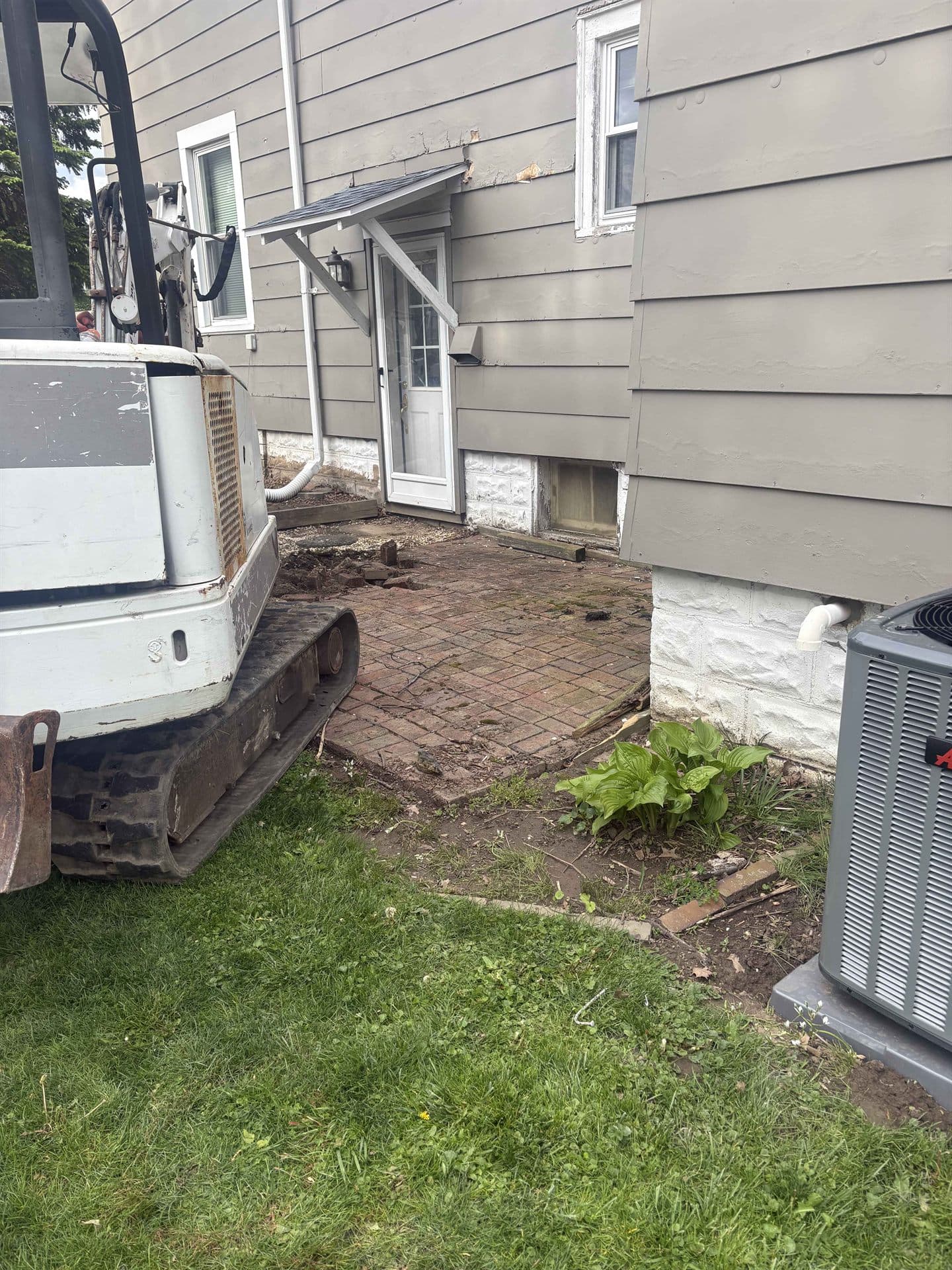 A mini excavator positioned next to an old brick patio for demolition