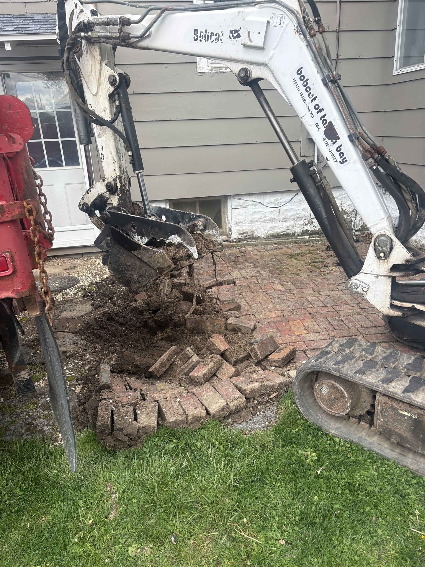 An excavator tearing out an old brick paver patio