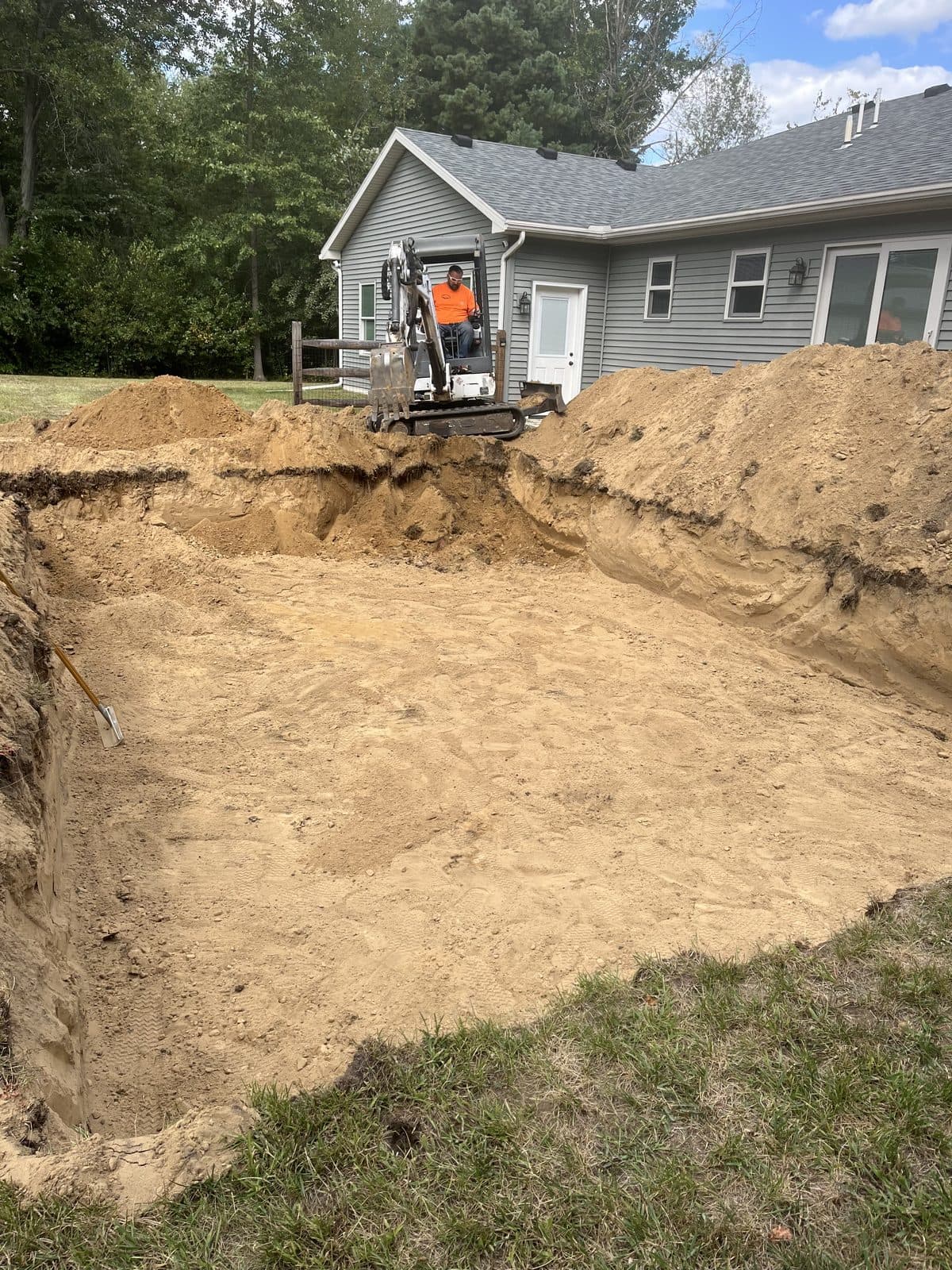 A skid steer digging out a foundation beside a house