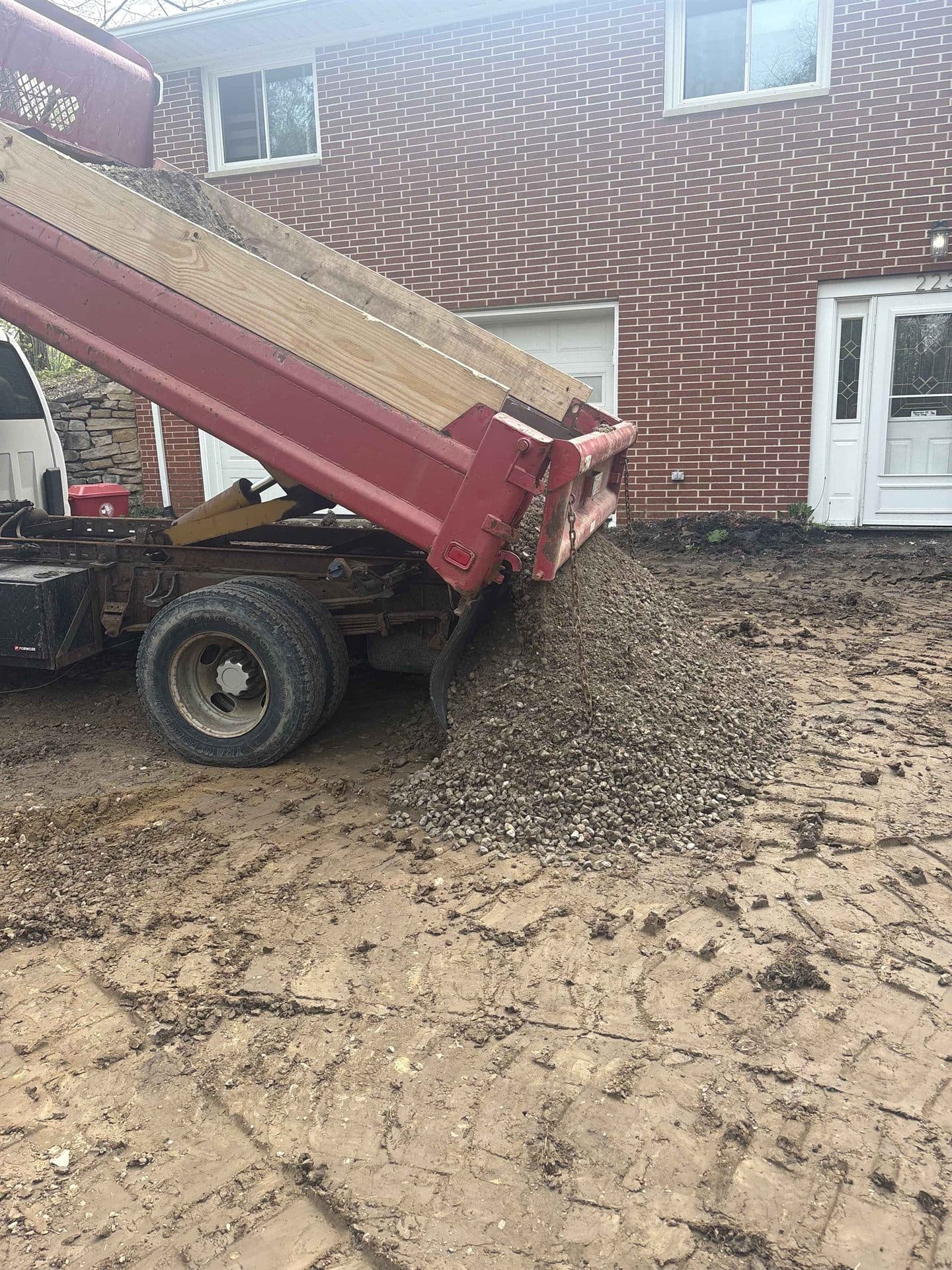 A dump truck unloading a load of gravel beside a house