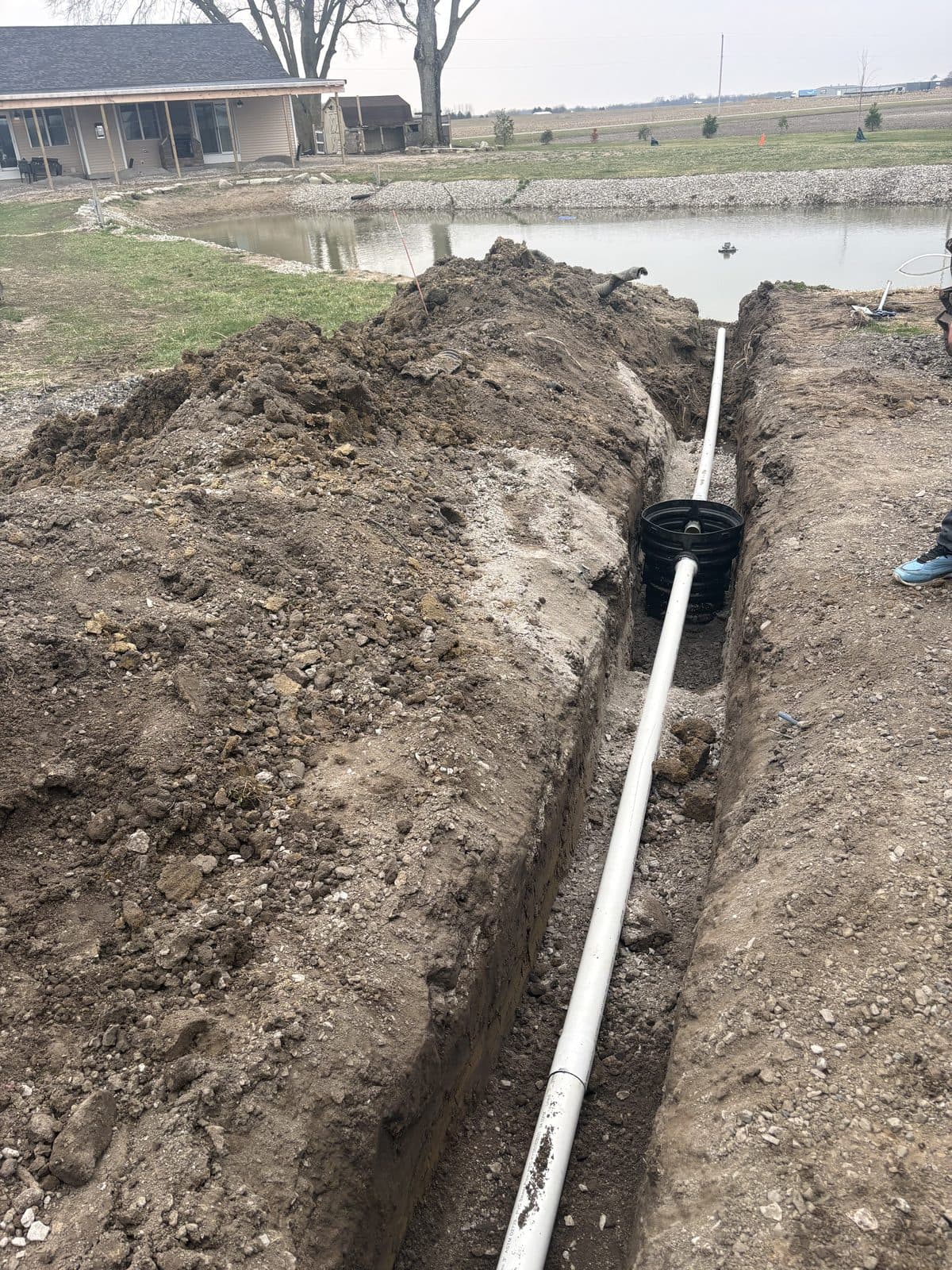 Corrugated drainage pipe laid in a freshly dug trench across a yard